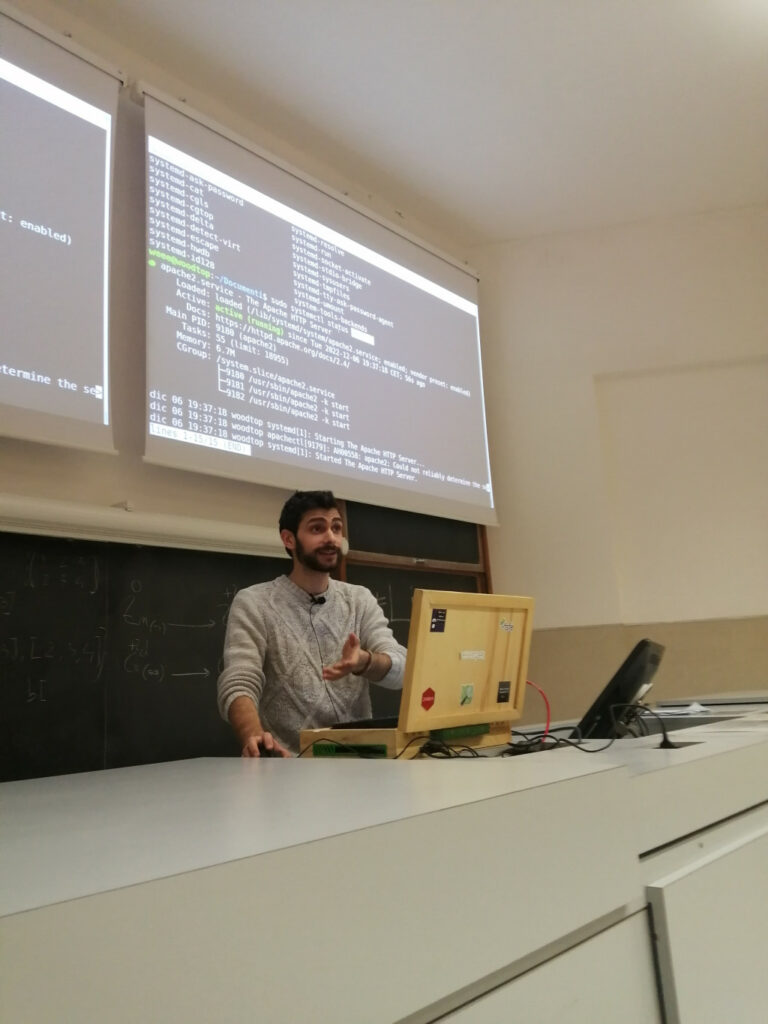 Valerio Bozzolan alla cattedra di un'aula mentre presenta una schermata di status di systemd